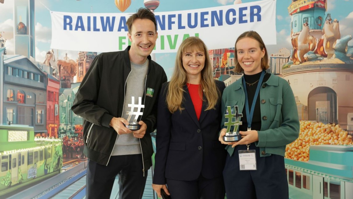  YouTuber Tobias Foltin, InnoTrans Director Kerstin Schulz and Heather Lewis stand in front of a colorful wall with awards in their hands.