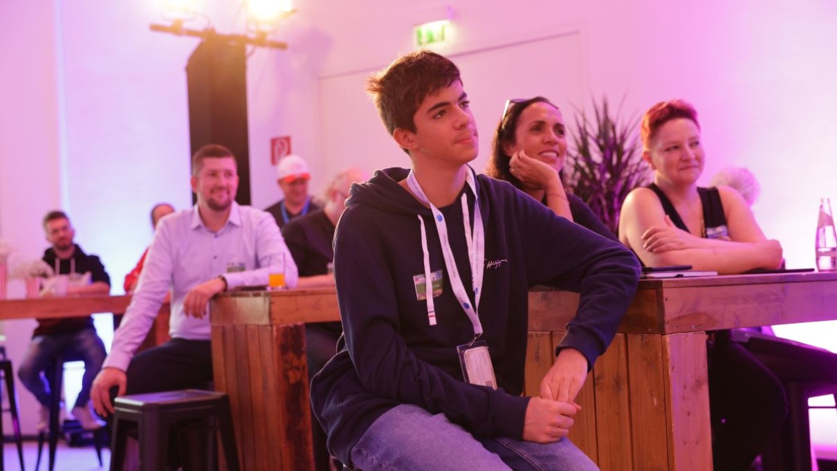  Adam El Rafey sits at a table in the audience and listens to a speech.